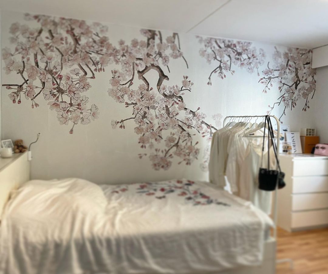 Soveværelse med hvide sengetøj, blomstret vægkunst og tøjstativ med hvidt tøj.