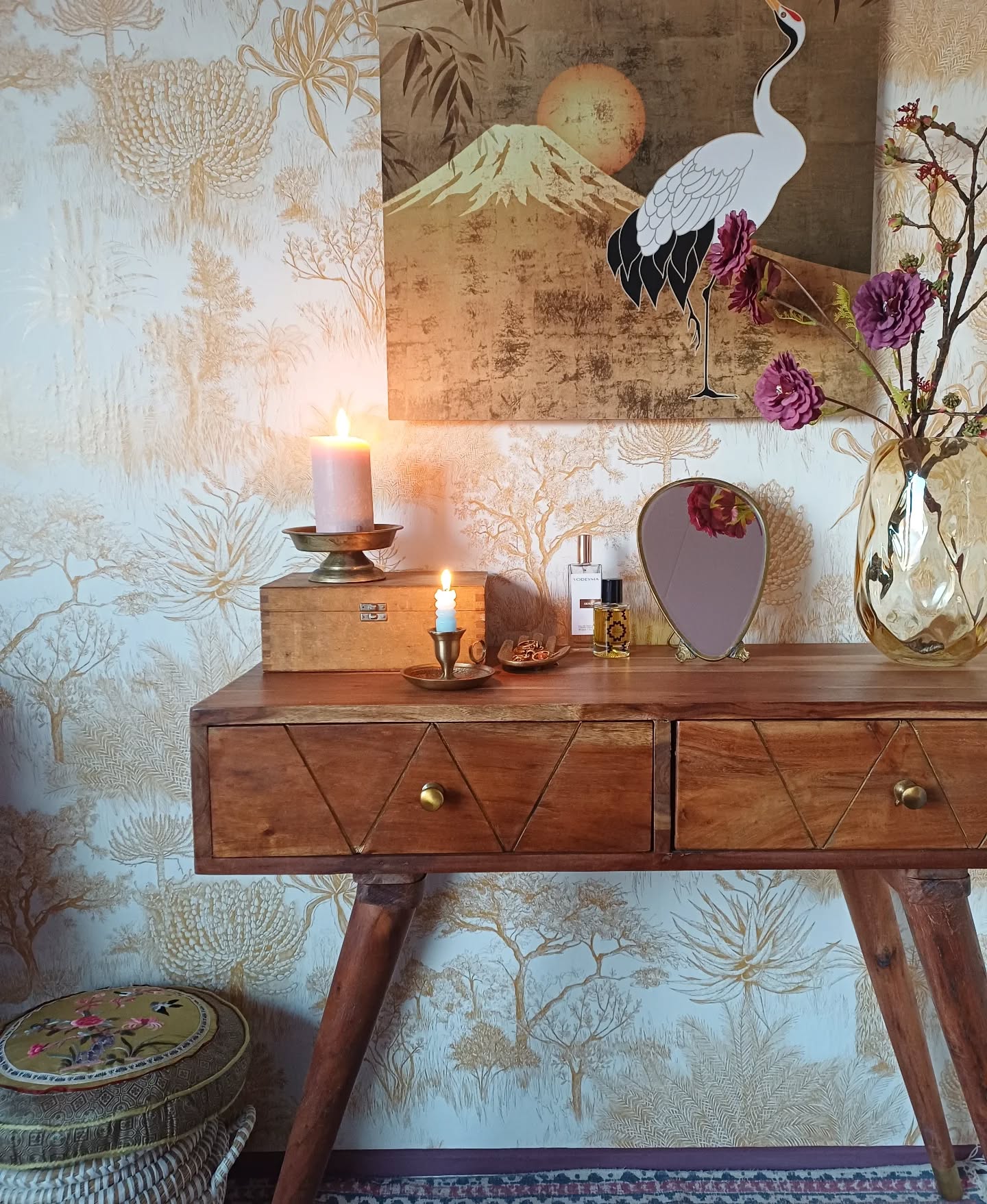 Wooden vanity with two lit candles, a crane painting, and a vase of flowers.