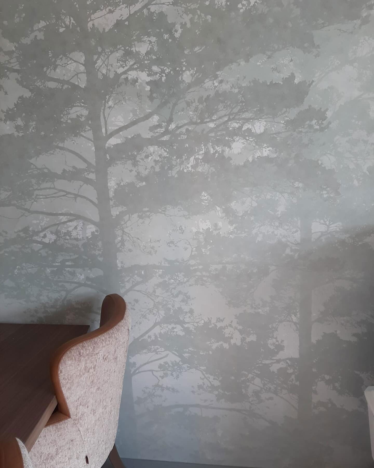 Zbliżenie ściany z tapetą o tematyce drzew i krzesła.