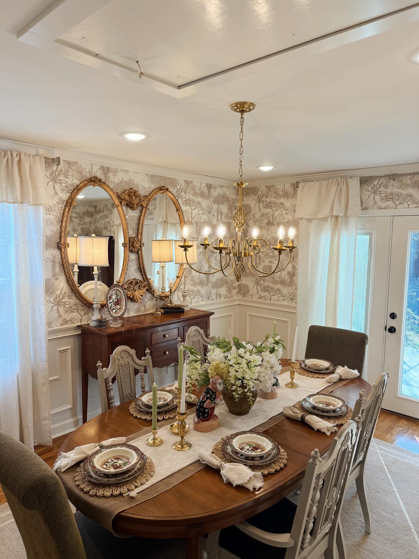 Elegant dining room table set for a meal, featuring a floral centerpiece, gold chandelier, and ornate mirrors.