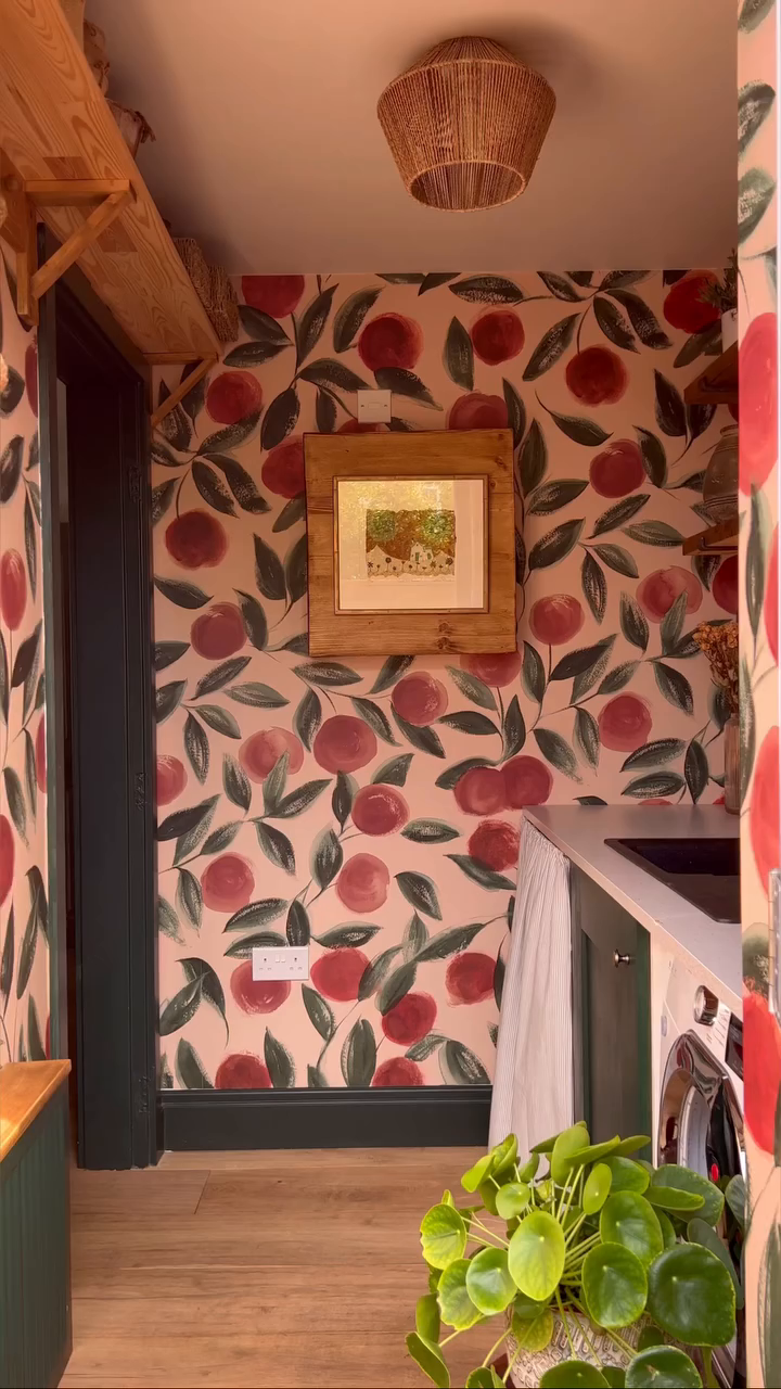 A cozy laundry room with peach-themed wallpaper, wooden floors, and a woven light fixture.