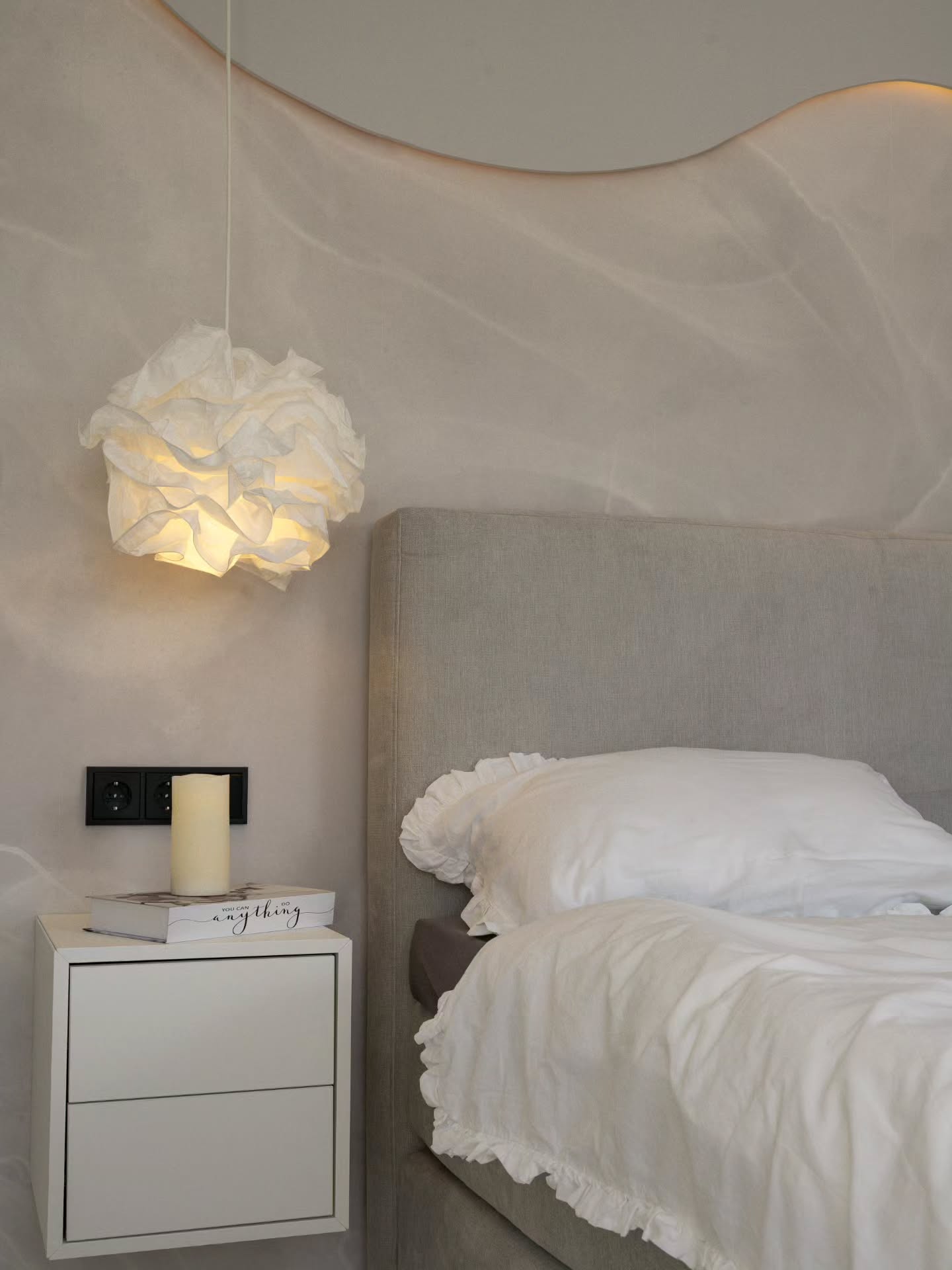 Scène de chambre avec une literie blanche à volants, une table de chevet et une suspension en forme de nuage.