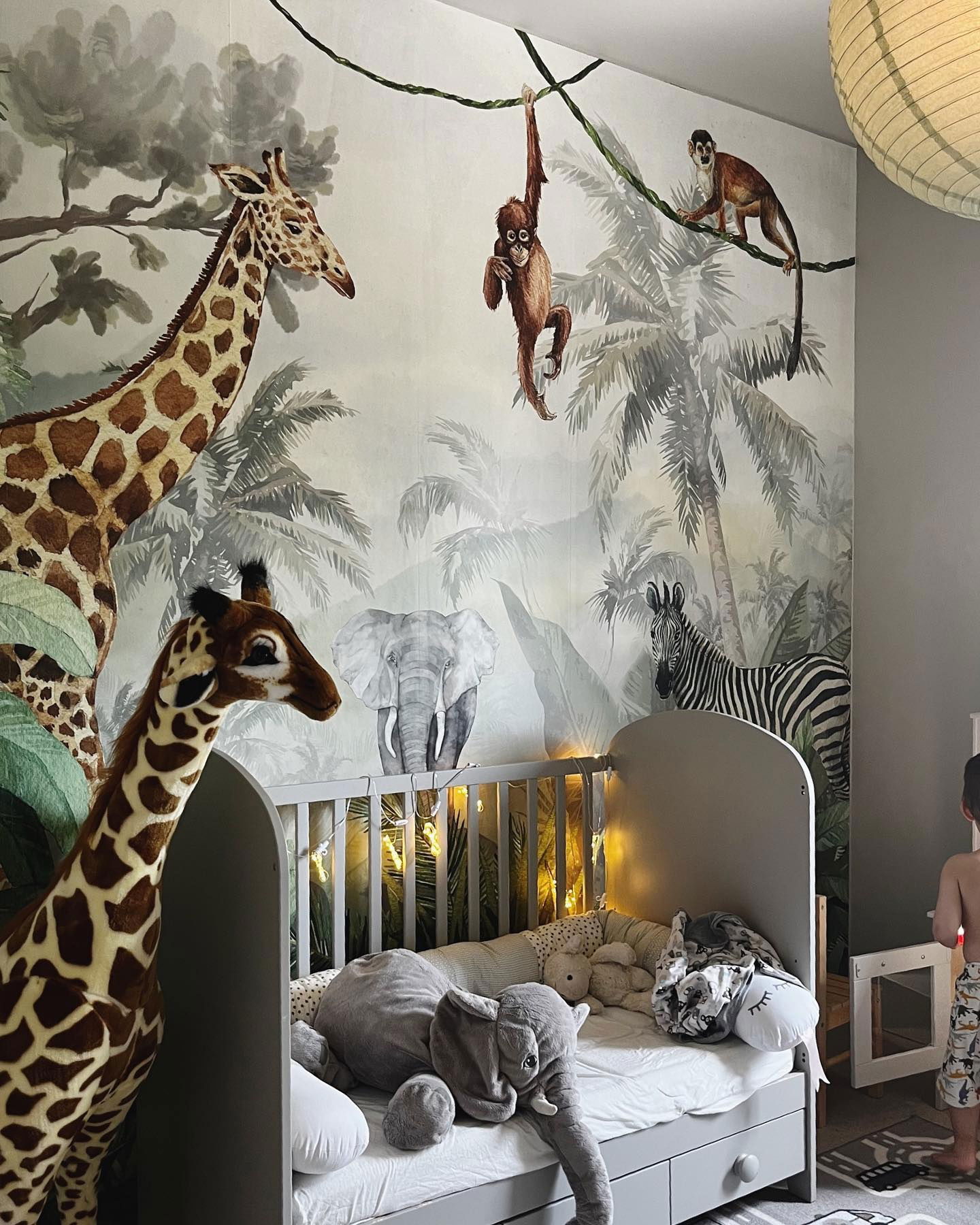 Kinderzimmer mit Dschungel-Wandbild, grauem Kinderbett und Stofftieren.