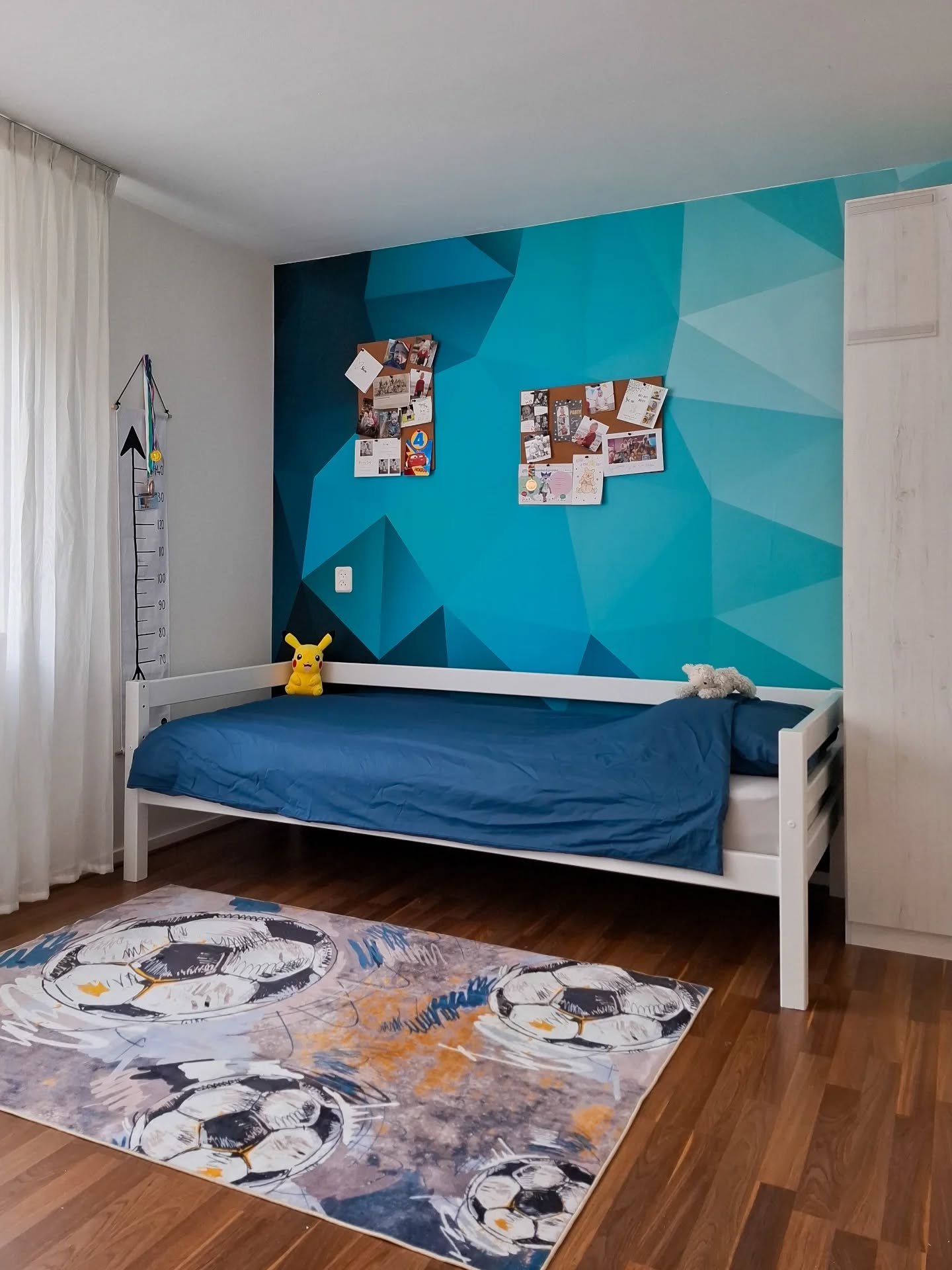 Chambre d'enfant avec un mur géométrique bleu, un lit blanc et un tapis de ballon de soccer.