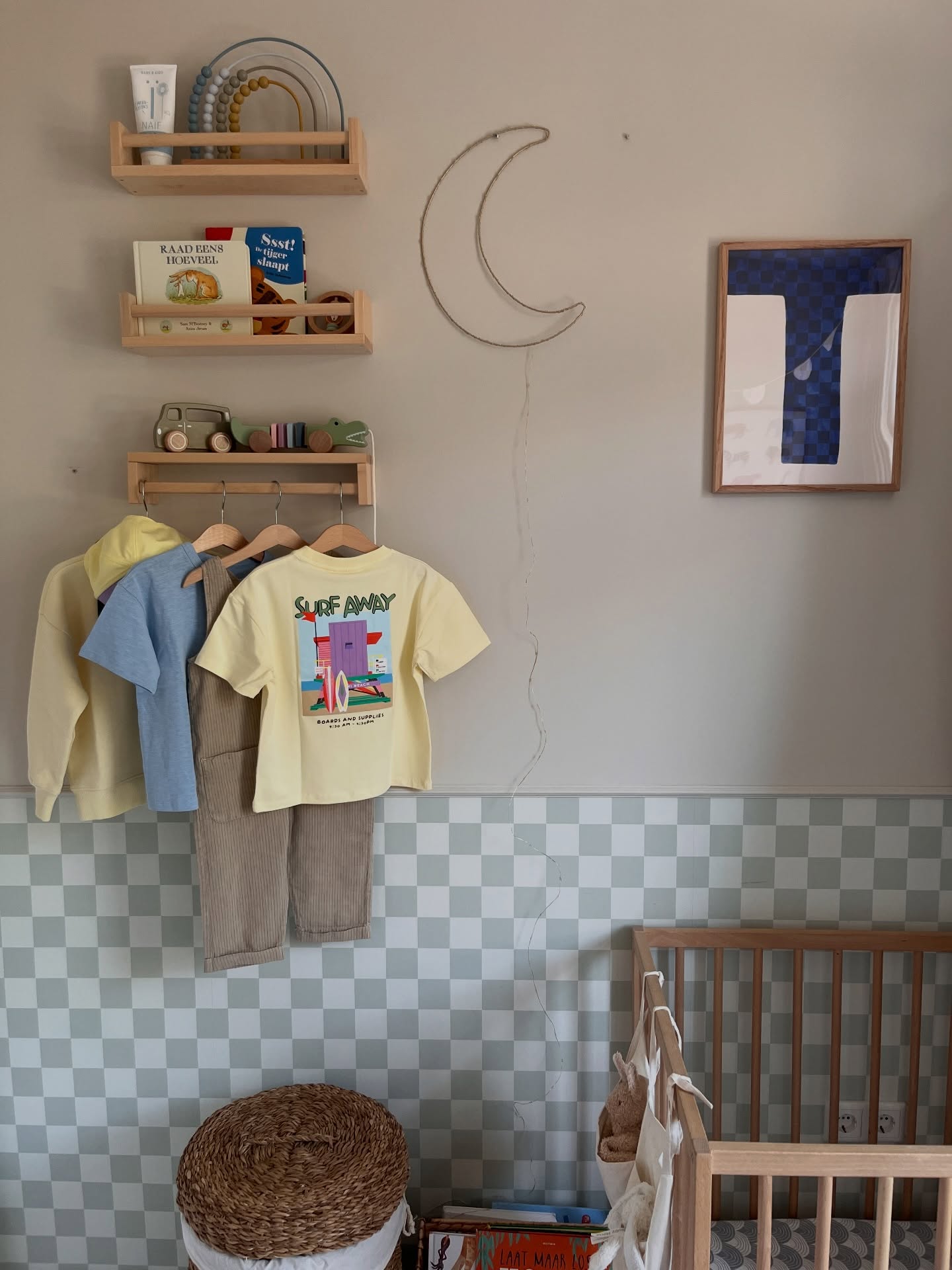 Children's clothes hang on a rack in front of a checkered wall, with shelves above displaying toys and books.
