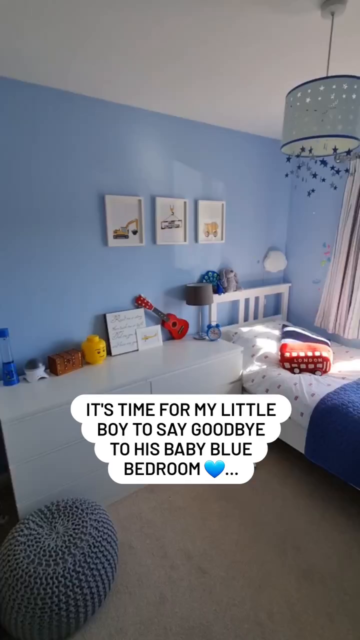 Child's blue bedroom with white furniture, construction vehicle art, and London bus pillow.