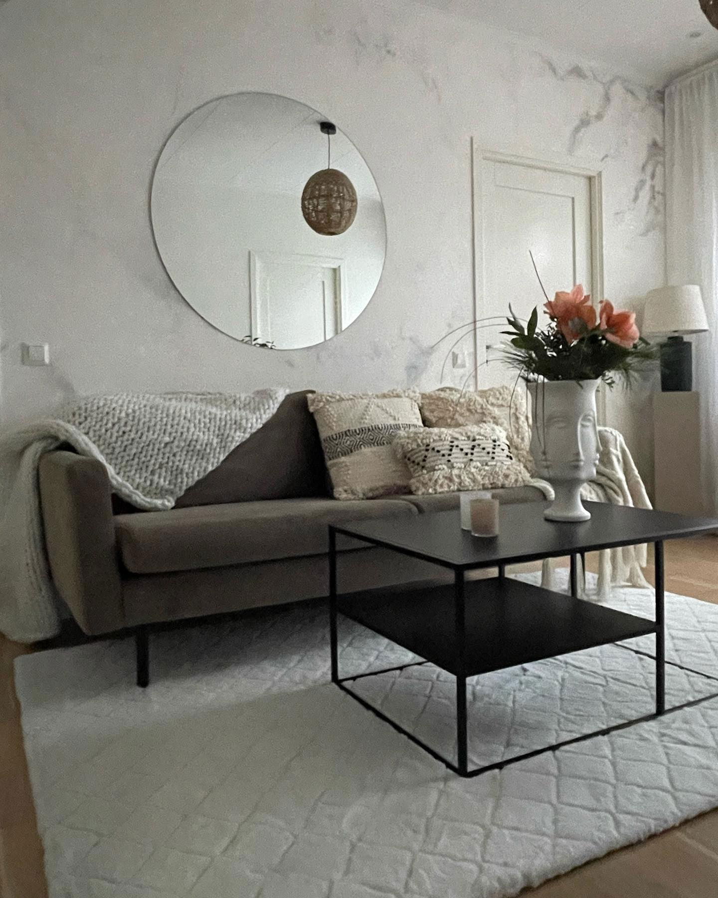 Living room with brown sofa, throw pillows, black coffee table, and round mirror.