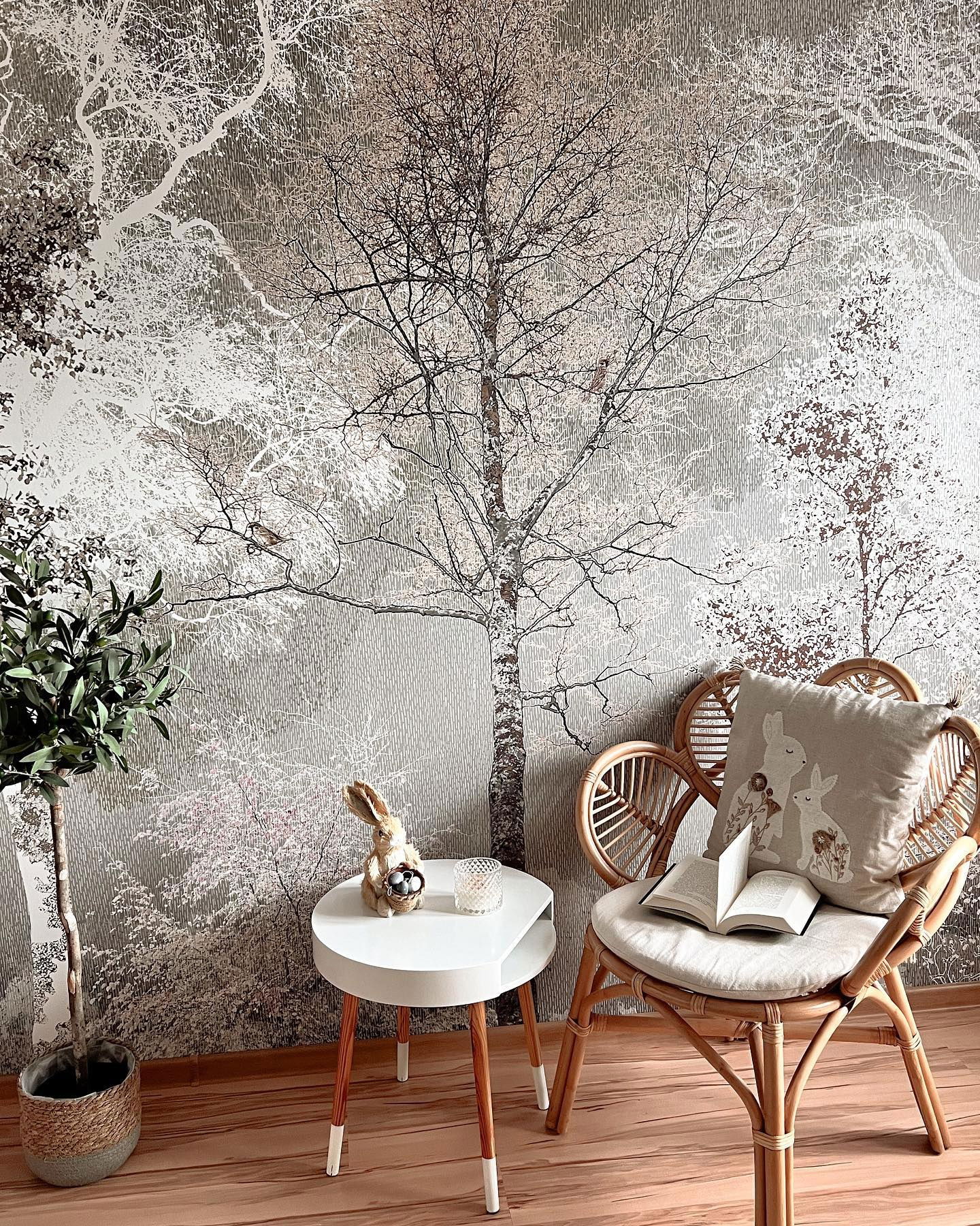 Cozy reading nook with rattan chair, book, bunny pillow, and forest wallpaper.
