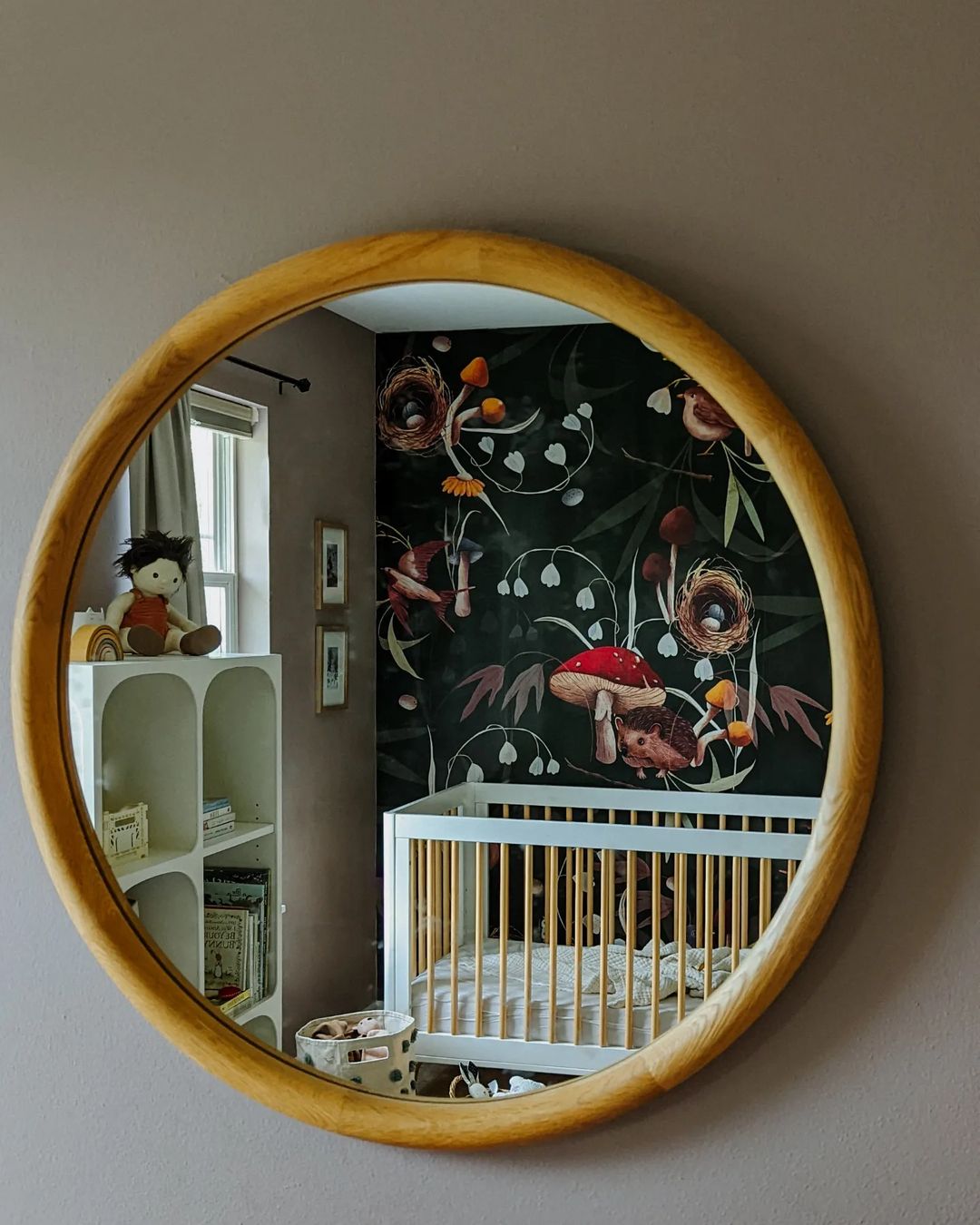 Spiegelung des Kinderzimmers in rundem Spiegel. Kinderbett, Bücherregal und Pilztapete sind sichtbar.