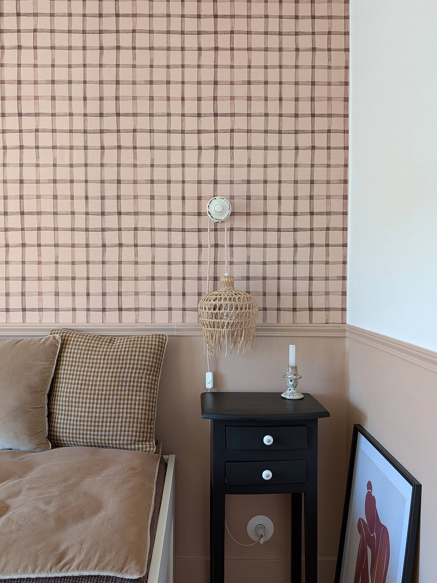 Bedroom with pink plaid wallpaper, a wicker pendant light, and a black nightstand with a framed picture.