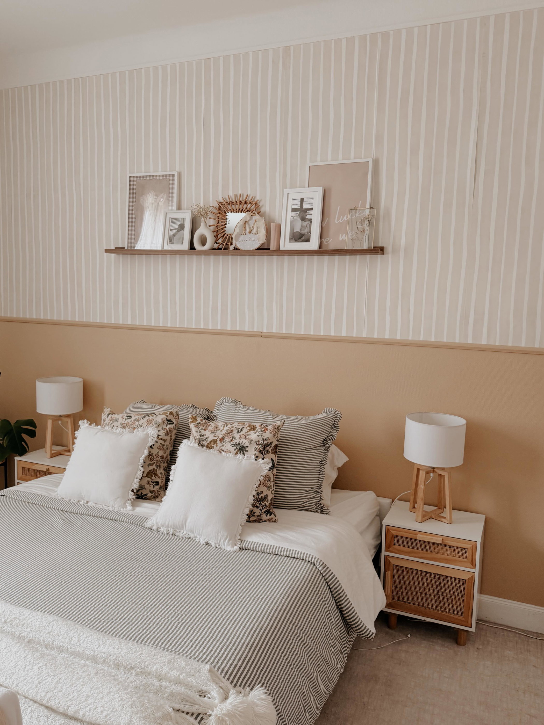 Bedroom with striped wallpaper, a bed with patterned pillows, and a wood-accented nightstand with a lamp.