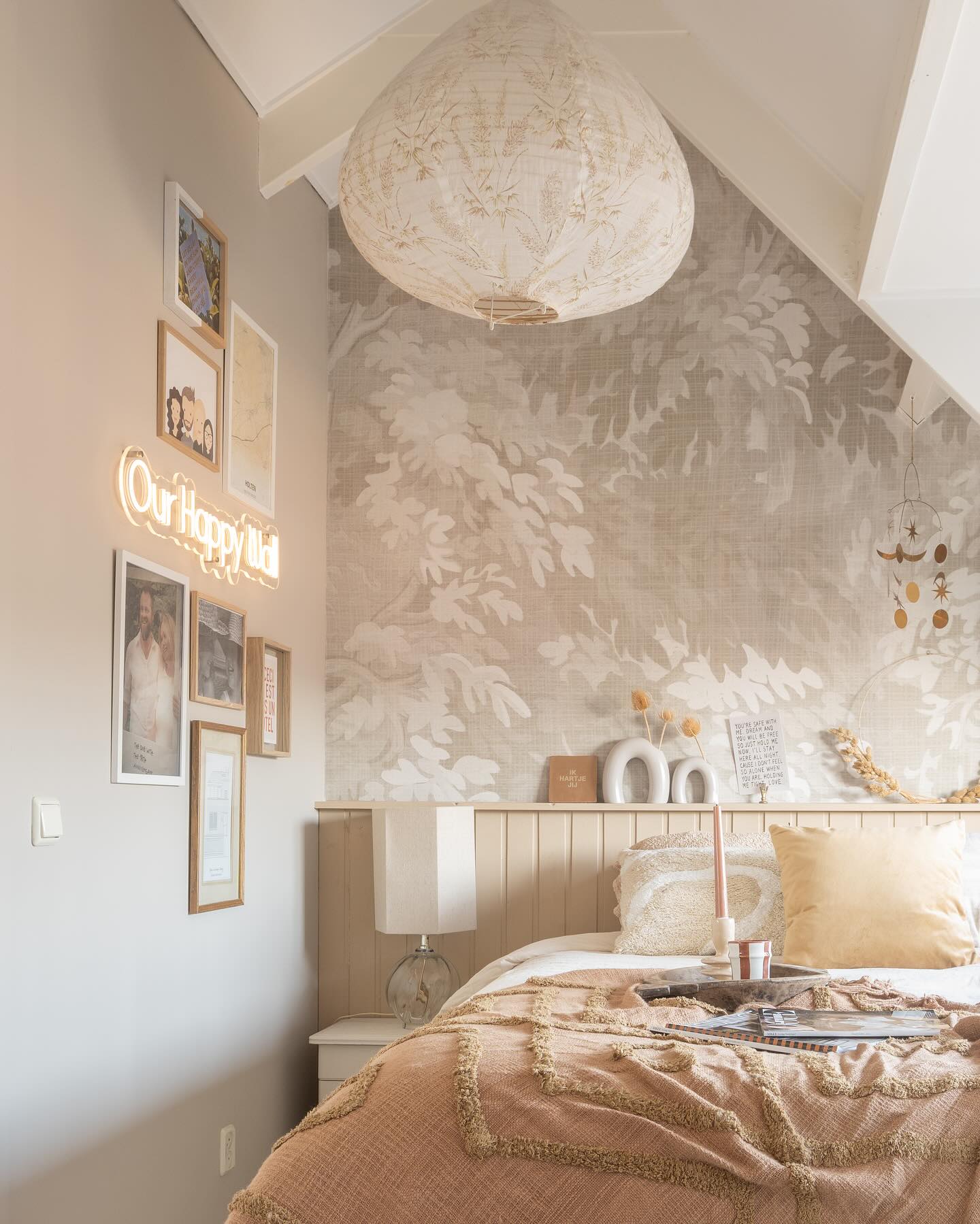 Cozy bedroom with floral wallpaper, bed with pink cover, and gallery wall.