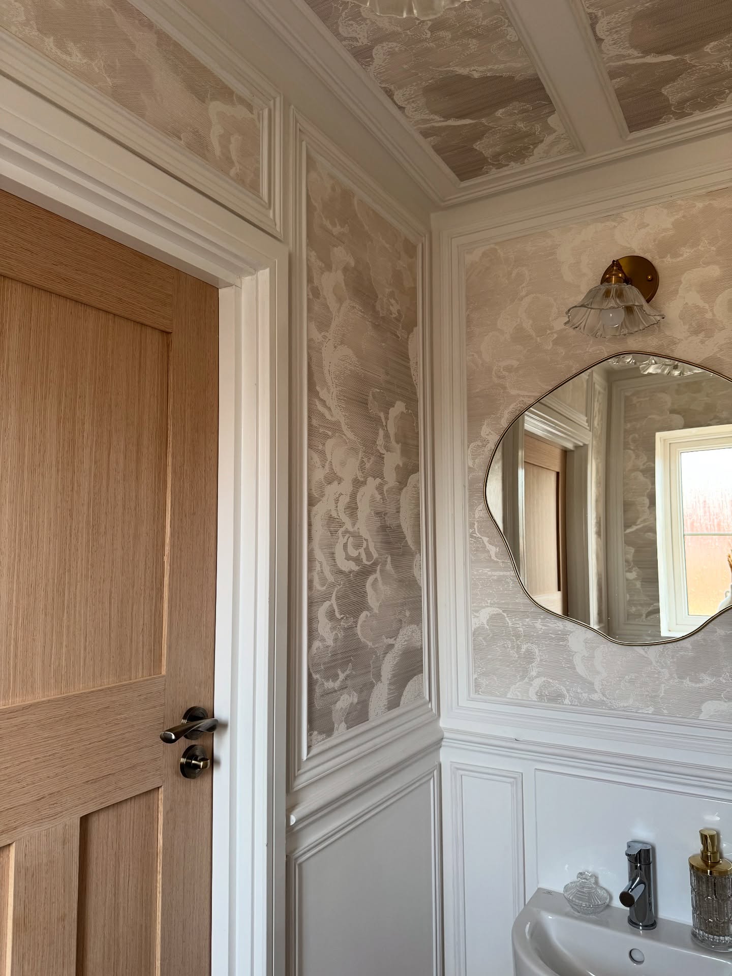 Bathroom corner with cloud wallpaper, white wainscoting, and light wood door.