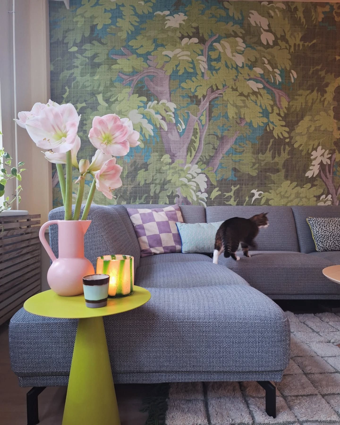 Living room with floral wallpaper, gray sofa, and a cat. A lime green side table holds flowers and candles.