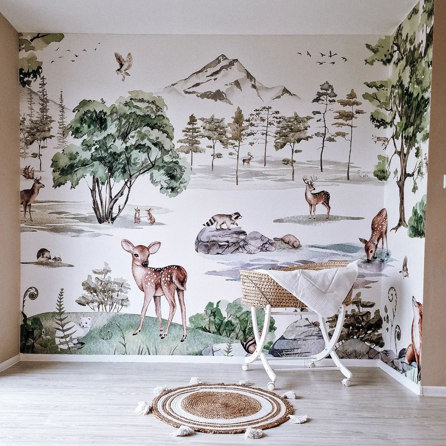 Chambre de bébé avec papier peint d'animaux de la forêt, couffin en osier avec couverture blanche et tapis rond en jute.