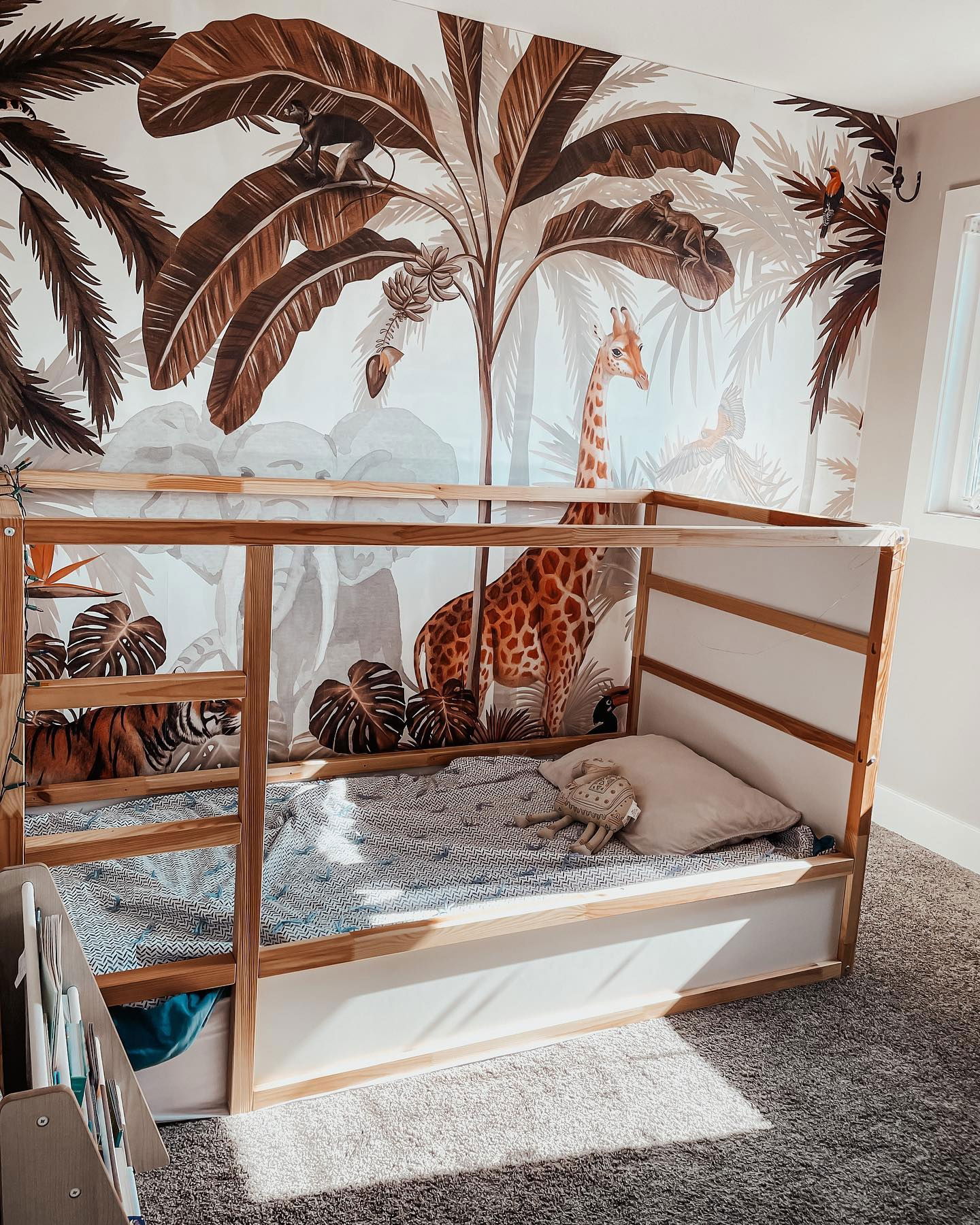 Kinderkamer met jungle muurschildering, houten bedframe, beddengoed met patroon en knuffel.