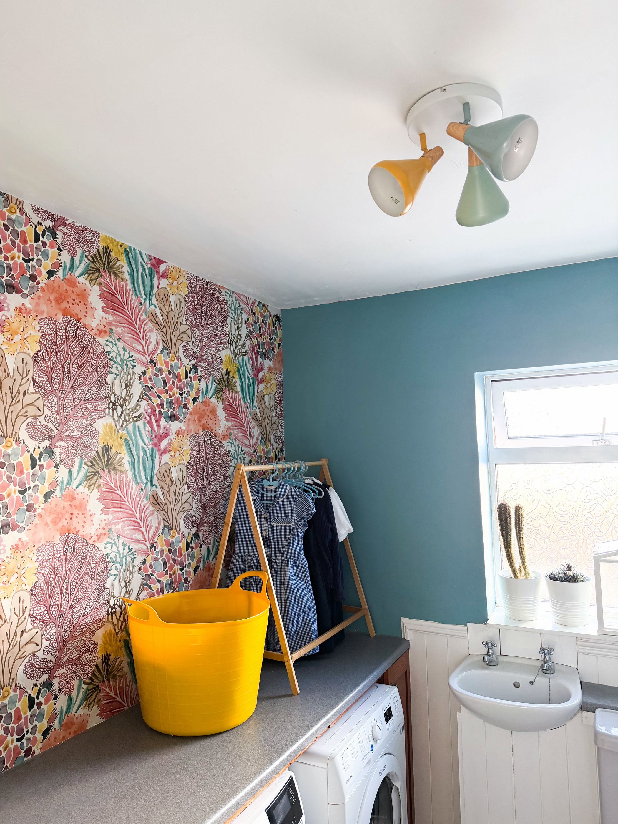 Laundry room with coral-print wallpaper, teal walls, yellow tub, and clothes rack.