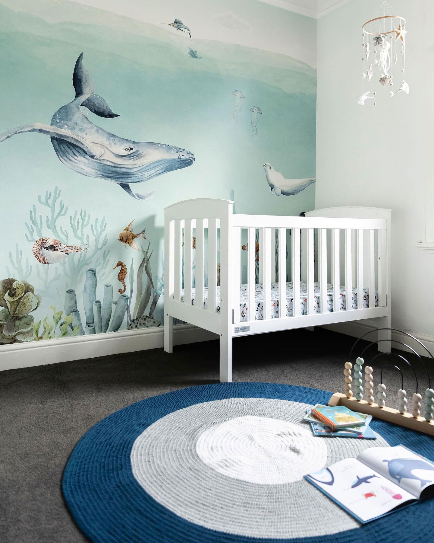 Nursery with white crib, ocean-themed mural, and blue and white round rug.