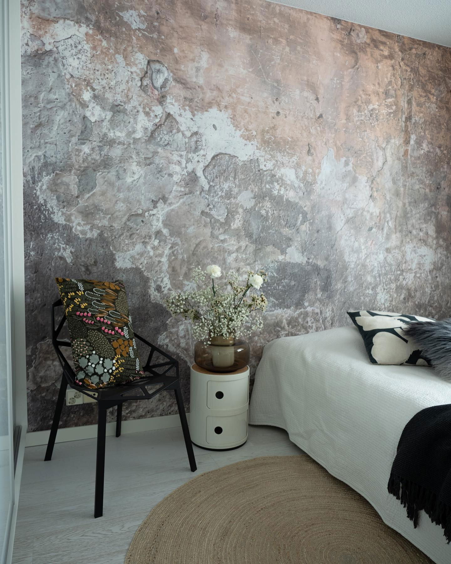 Bedroom with textured wall, black chair with patterned pillow, and round jute rug.