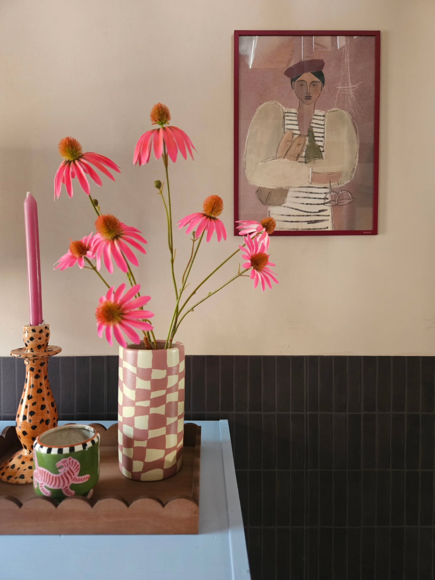 Mazzo di echinacea rosa in un vaso a scacchi accanto a un portacandele animalier.