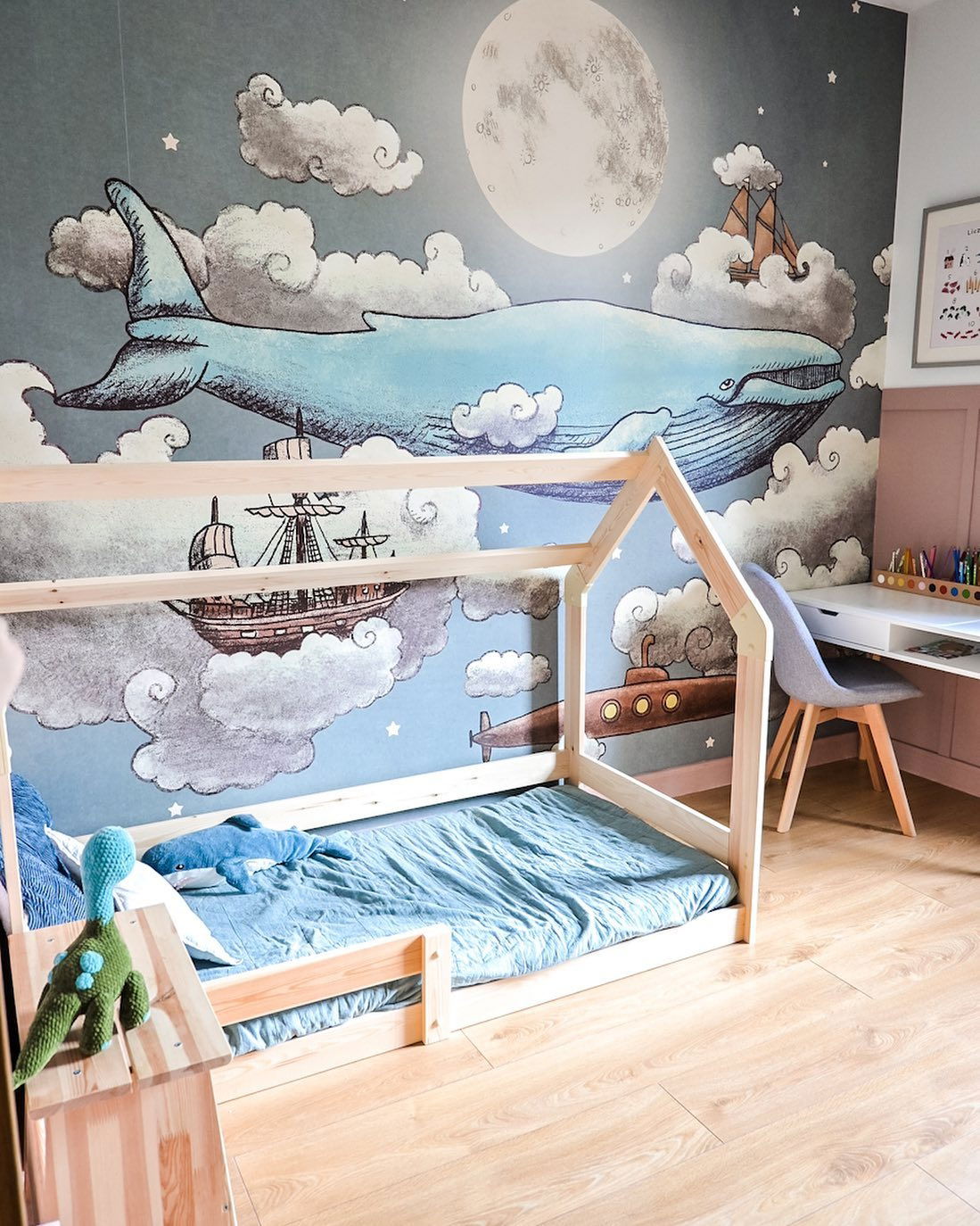 Child's room with house frame bed, blue bedding, and whimsical wallpaper featuring a whale, moon, and clouds.
