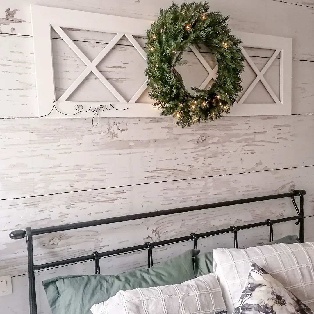 Slaapkamer met zwart metalen bed, kussens en witte houten wanddecoratie met krans.