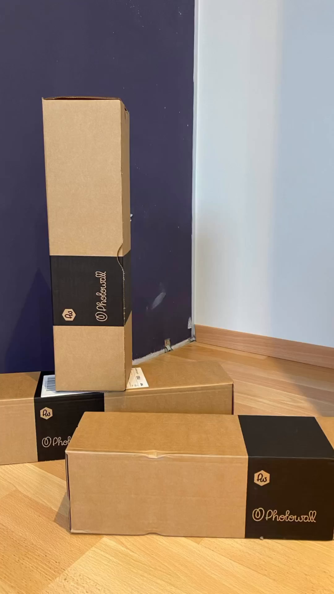 Several Photowall boxes on a wood floor against a blue and white wall.