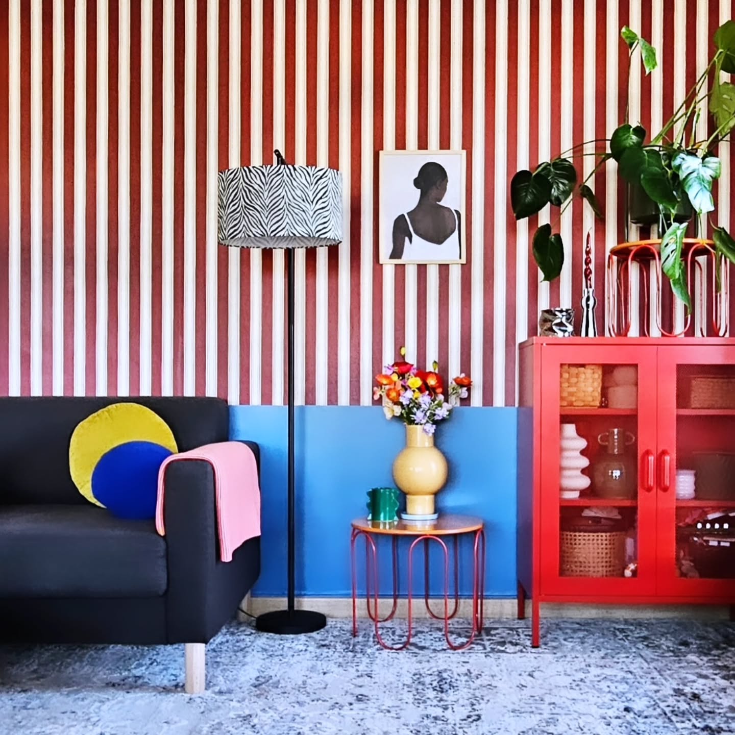 Living room with striped wallpaper, black sofa, and red cabinet.