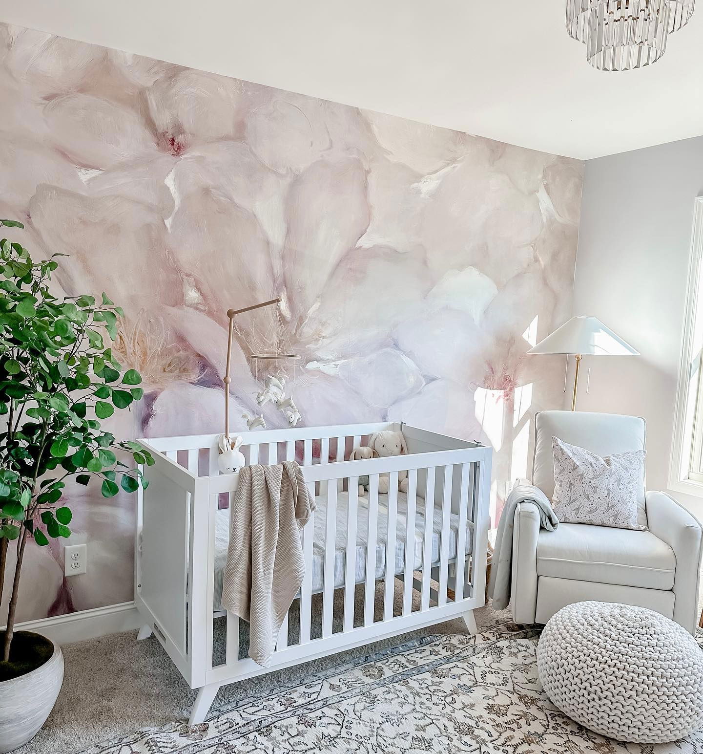 Kinderzimmer mit weißer Wiege, Blumentapete und weißem Schaukelstuhl.