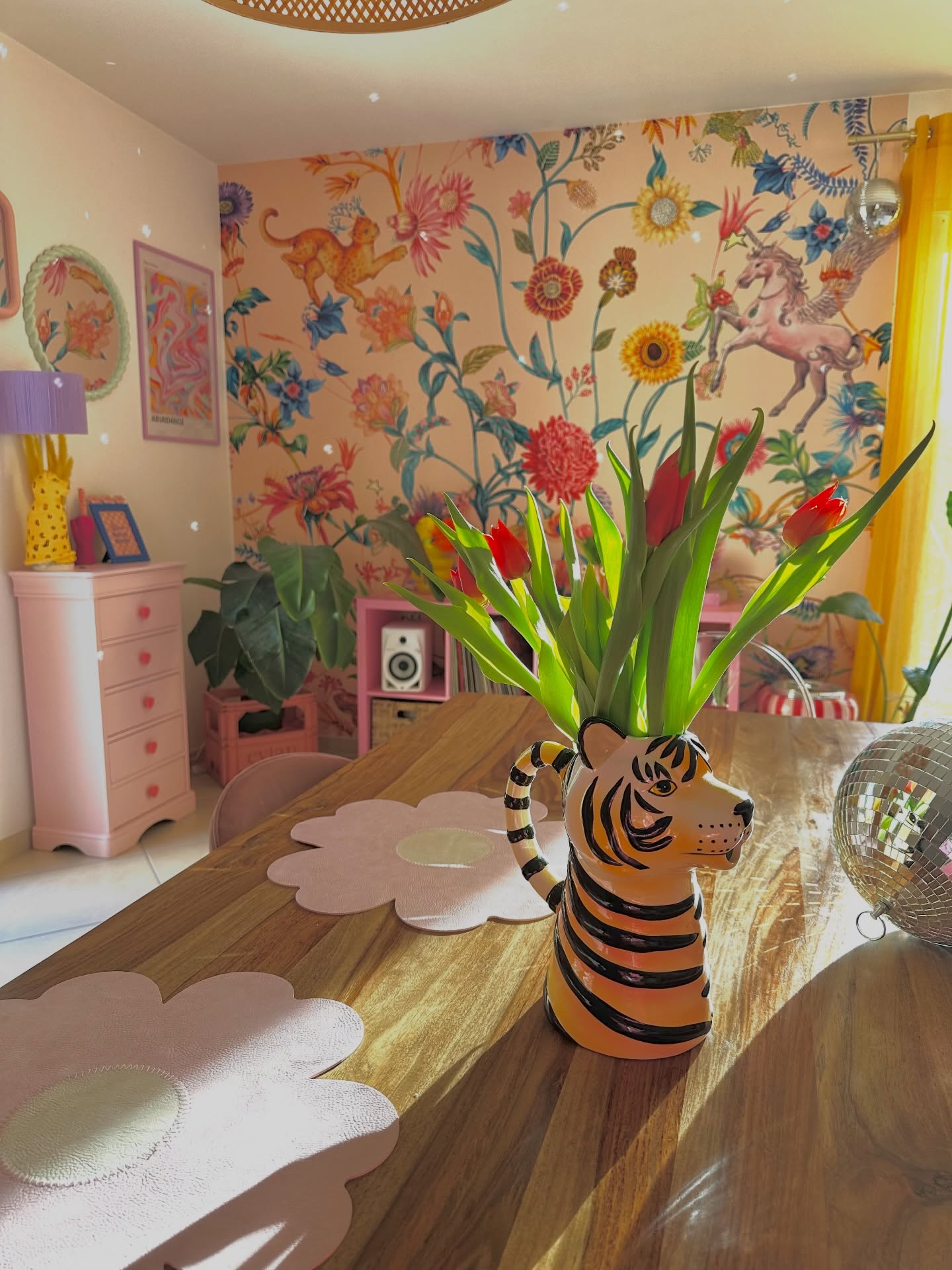 Tiger-shaped vase with tulips on a wooden table, with floral wallpaper and pink furniture in the background.
