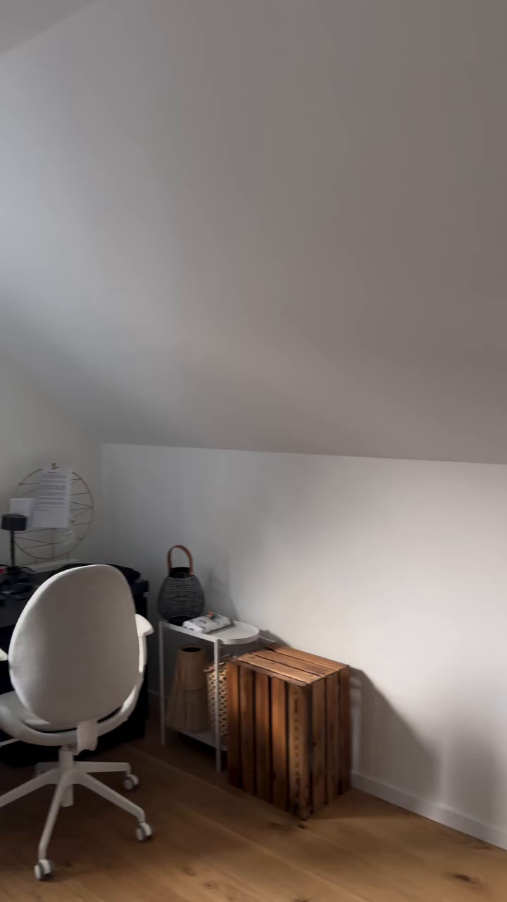 Attic office space with white chair, desk, side table, and wooden crate.