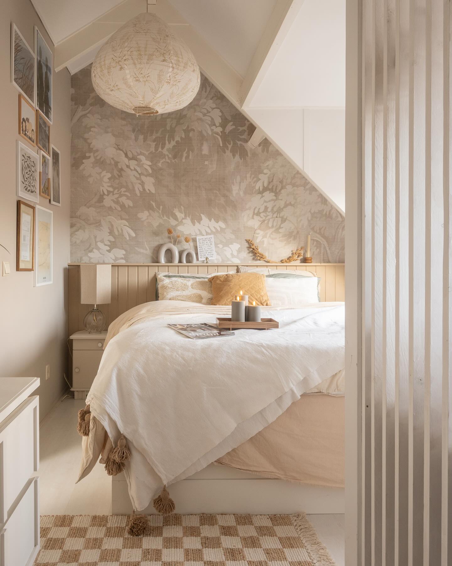 Cozy bedroom with white bedding, patterned wallpaper, and a woven pendant light.