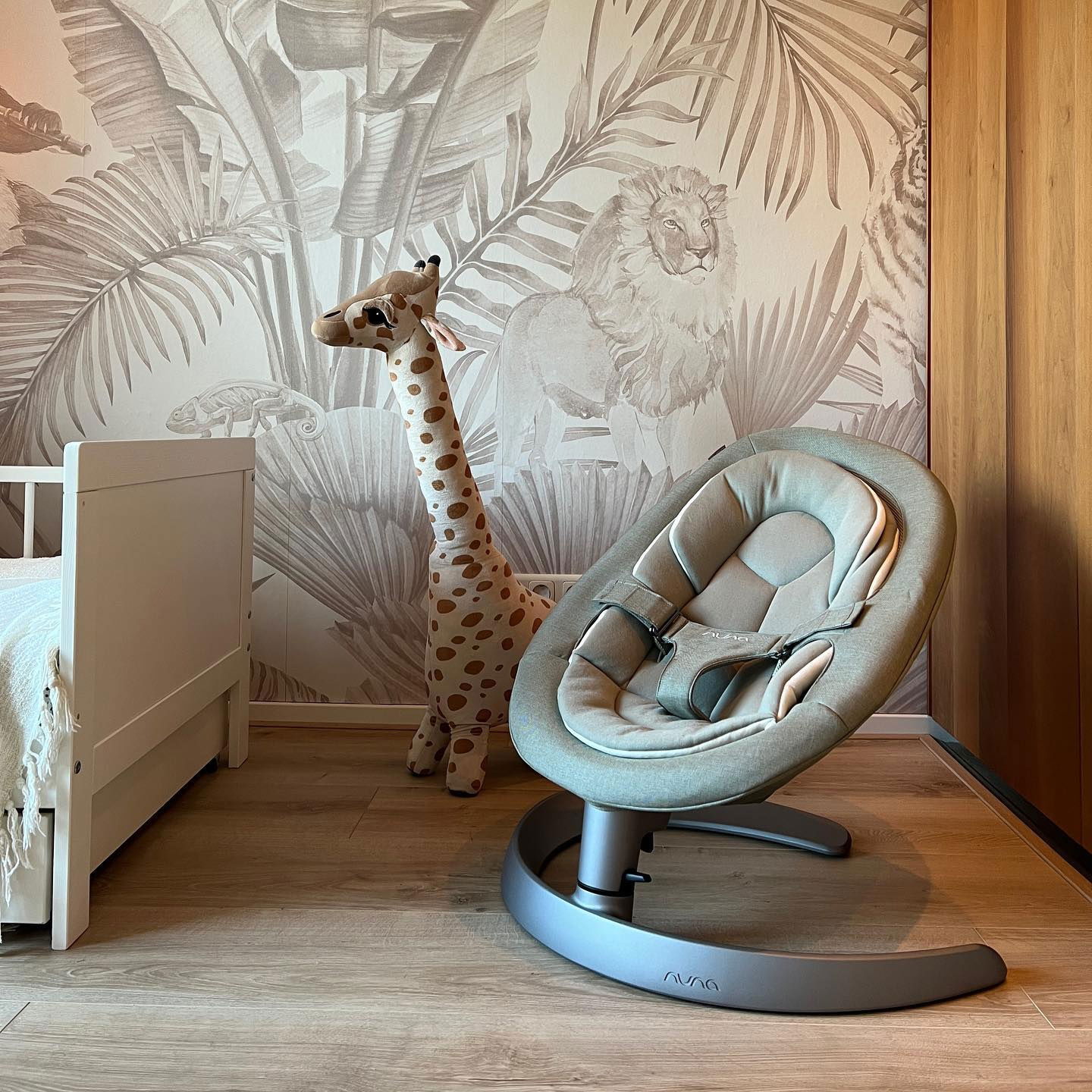 Siège bébé Nuna Leaf Grow dans une chambre d'enfant avec du papier peint jungle et un jouet girafe.