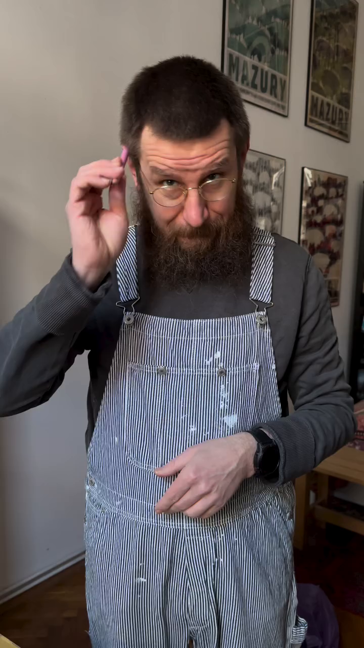 Bearded man in striped overalls puts pink earplug in ear.