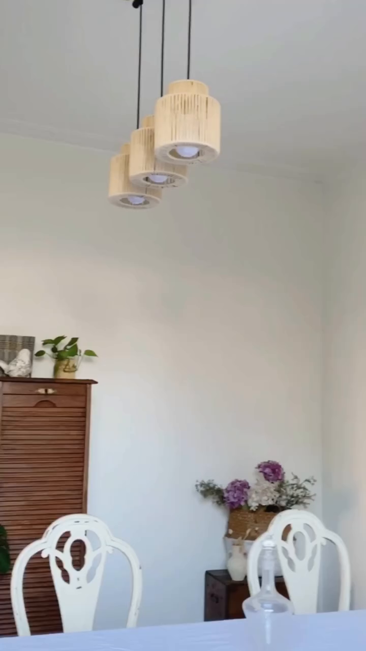 Dining room with three woven pendant lights, white chairs, and a wooden cabinet.