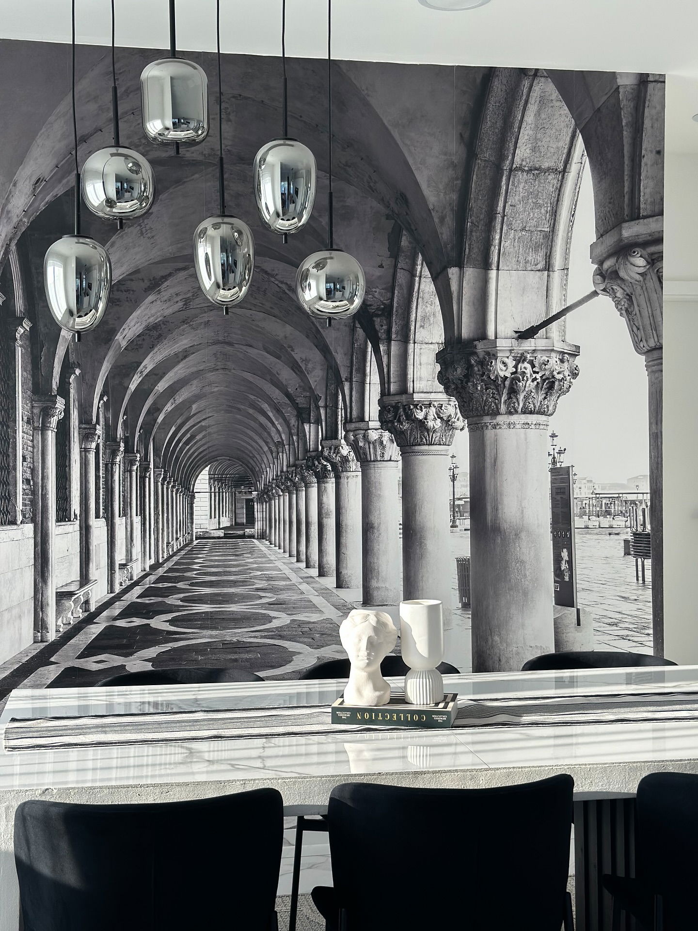 Innenraum mit verchromten Pendelleuchten, Wandgemälde des venezianischen Flurs, dekorative Büsten auf einem Marmortisch.