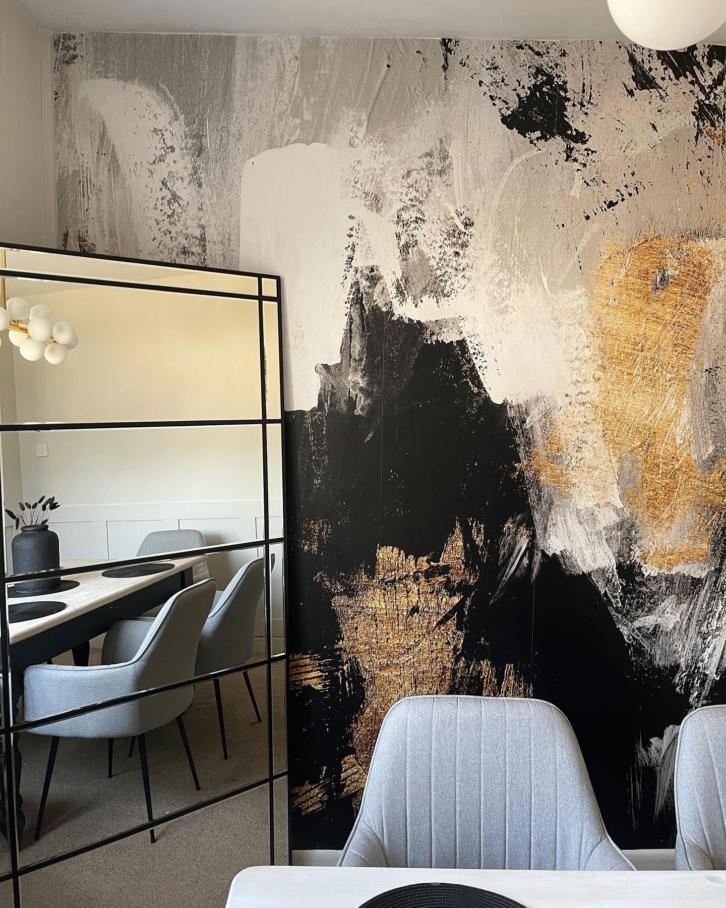 Dining room with abstract black, white, and gold wallpaper, reflected in a black framed mirror.