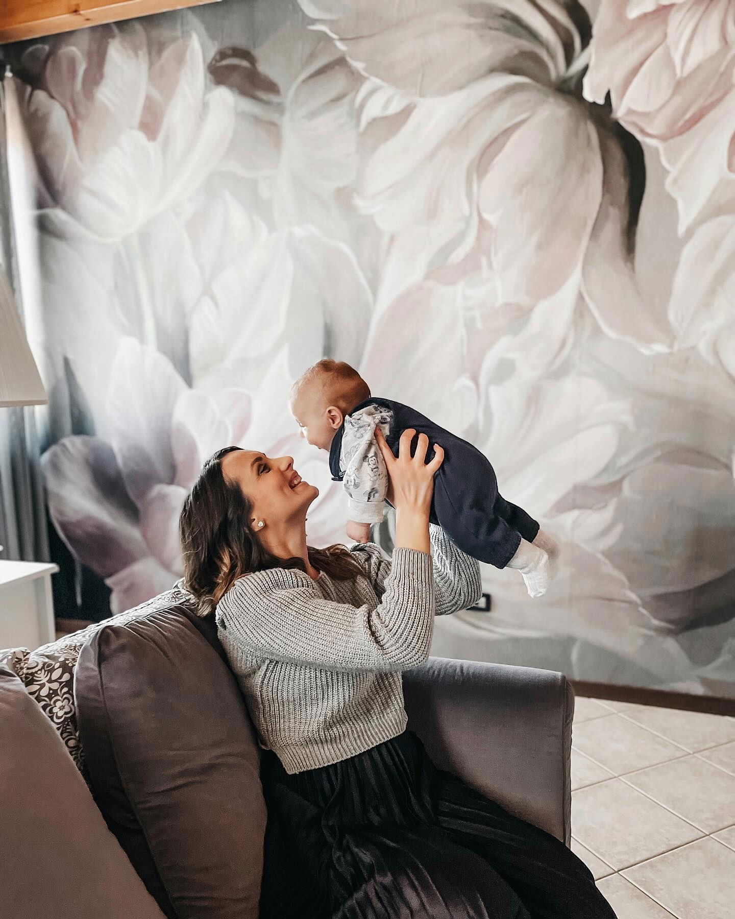 A woman holds a baby up in the air while sitting on a couch.