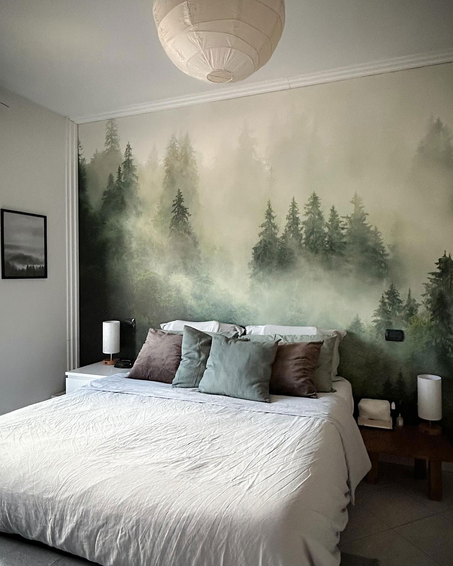 Schlafzimmer mit weißer Bettwäsche, braunen und grünen Kissen und einem Waldwandbild.