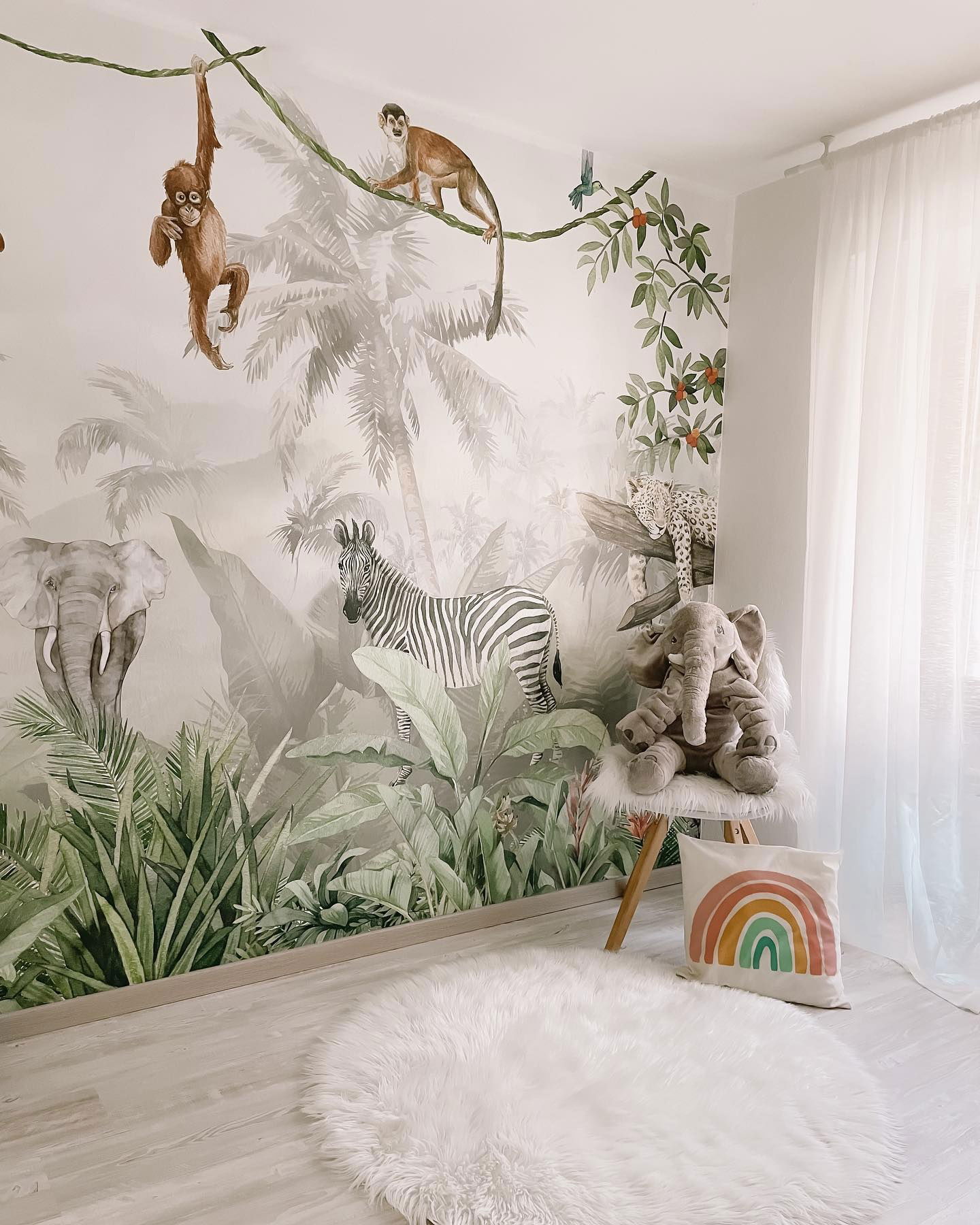 Child's room with jungle mural, stuffed elephant on stool, and rainbow pillow.