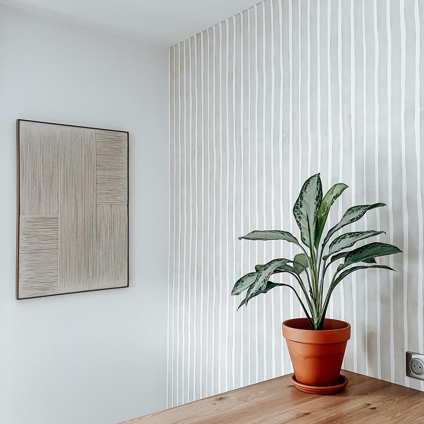 Minimalistische Zimmerecke mit gestreifter Tapete, gerahmter Kunst und Topfpflanze.