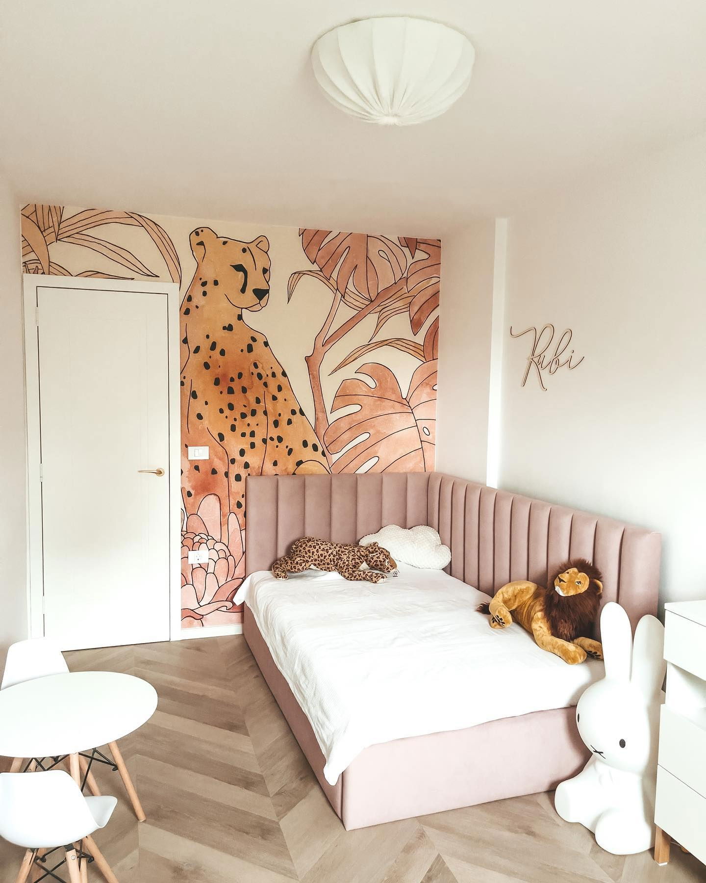 Child's bedroom with pink bed, animal mural, and stuffed animals.