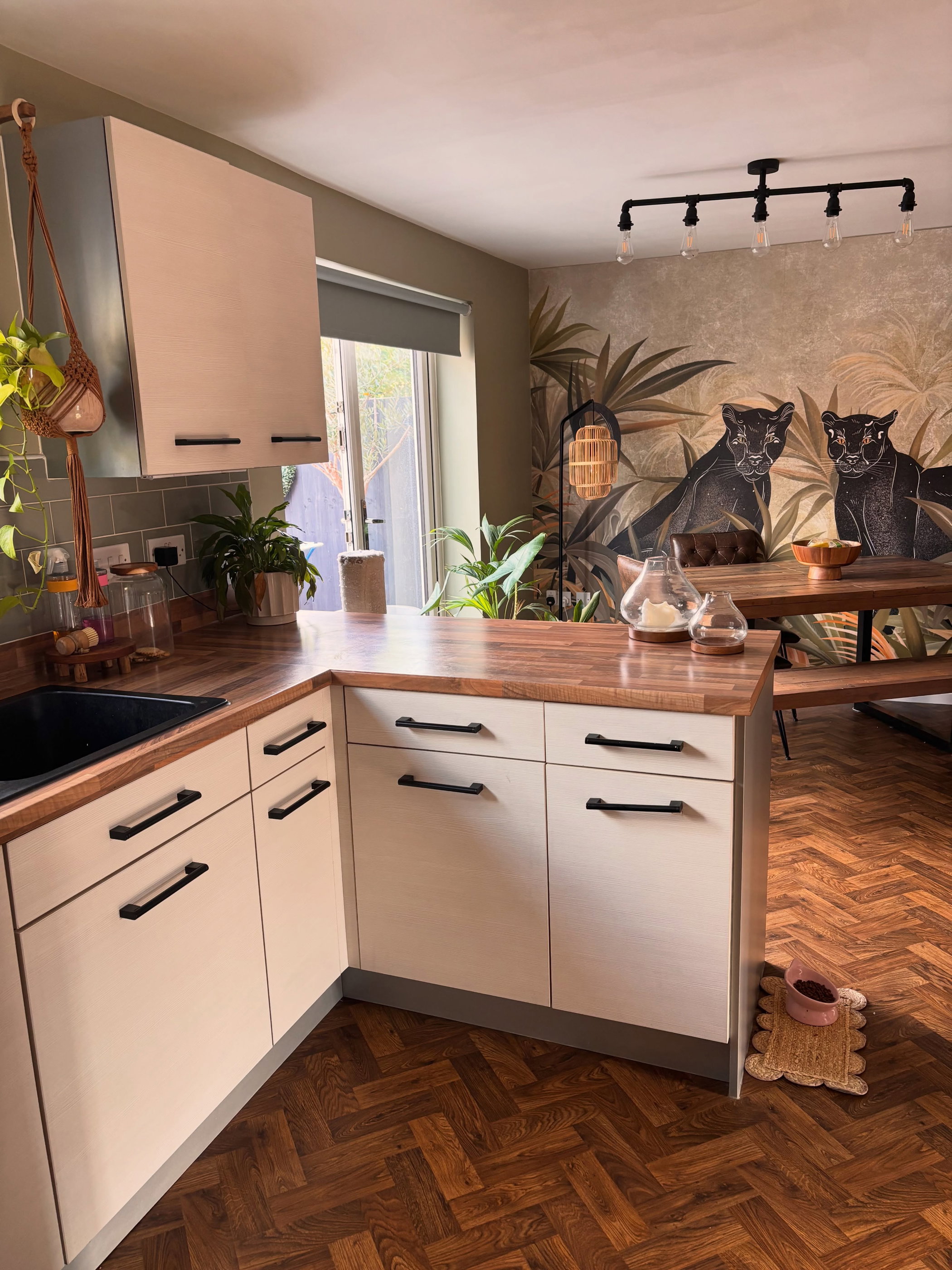 A kitchen with white cabinets, butcher block counters, and a jungle-themed mural with panthers.