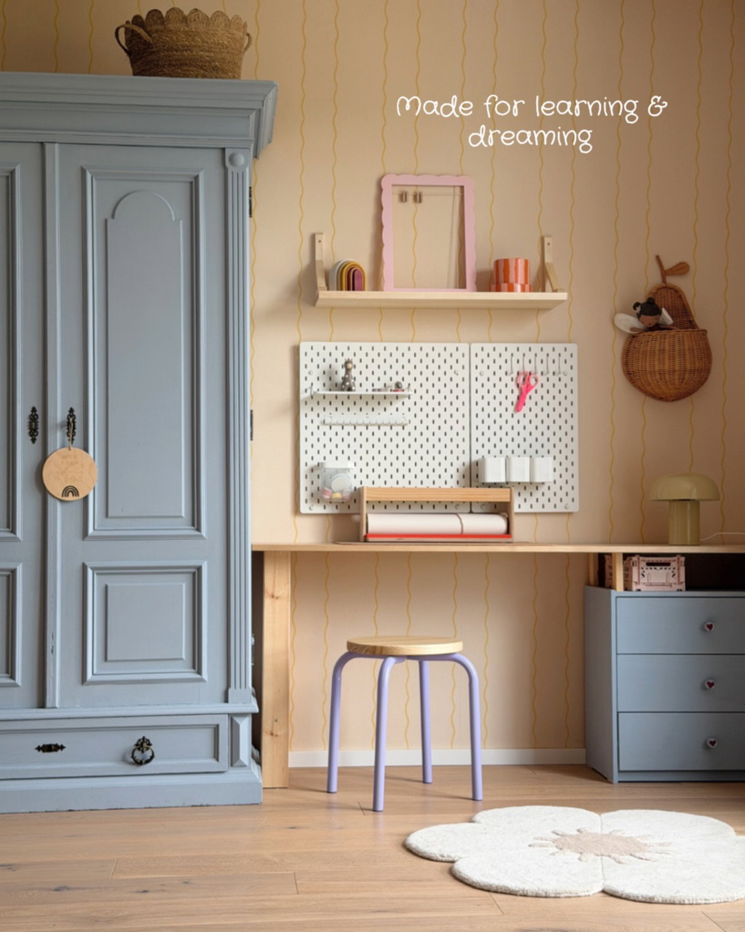 A light blue armoire and desk with pegboard storage and a light purple stool in a child's room.