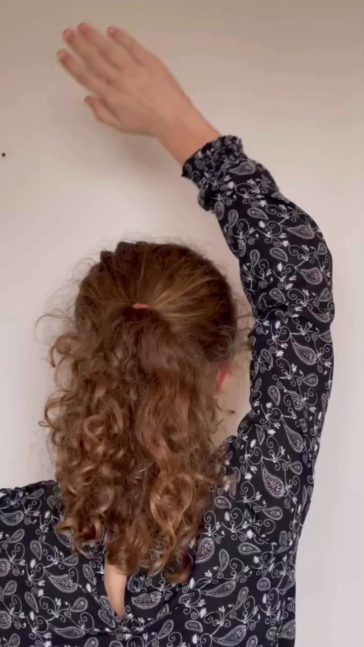 Back view of curly-haired person in paisley blouse with arm raised.