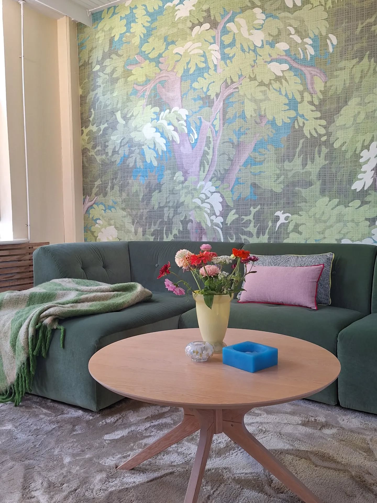 Living room with green sectional sofa, floral wallpaper, and a wood coffee table with flowers.