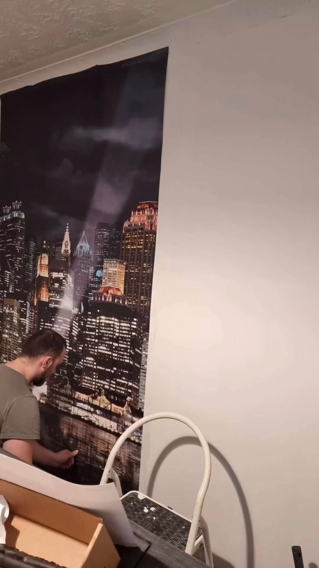 Man installing a New York City skyline wall mural. A white step ladder is nearby.