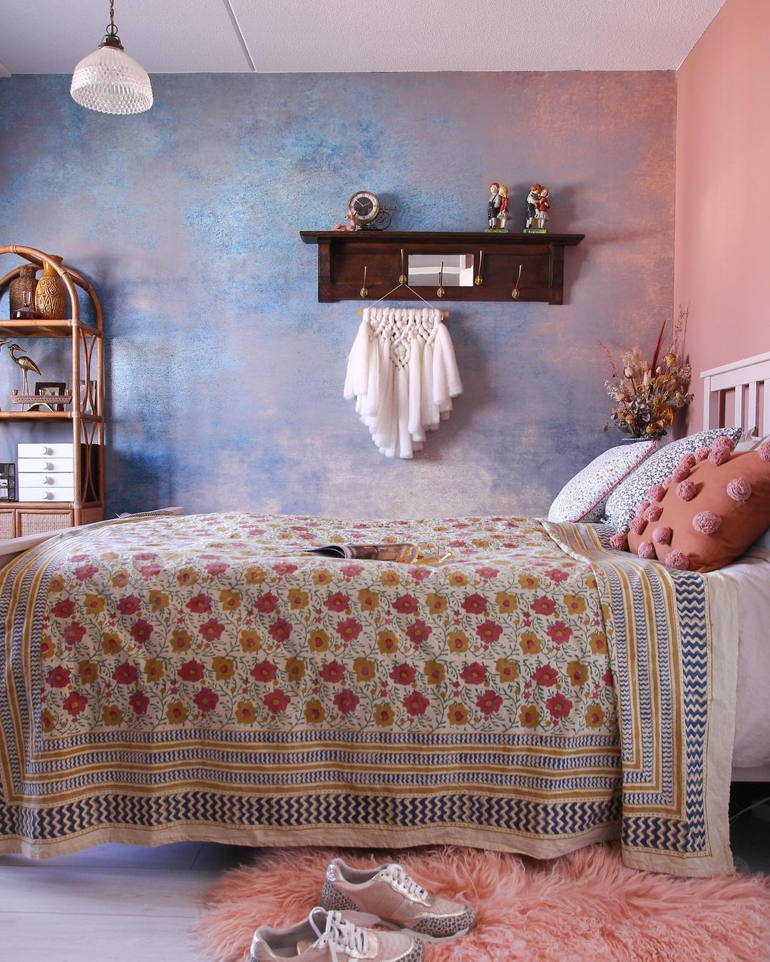Bohemian bedroom with floral quilt, pink shag rug, and blue textured wall. Shelf with macrame and decor.