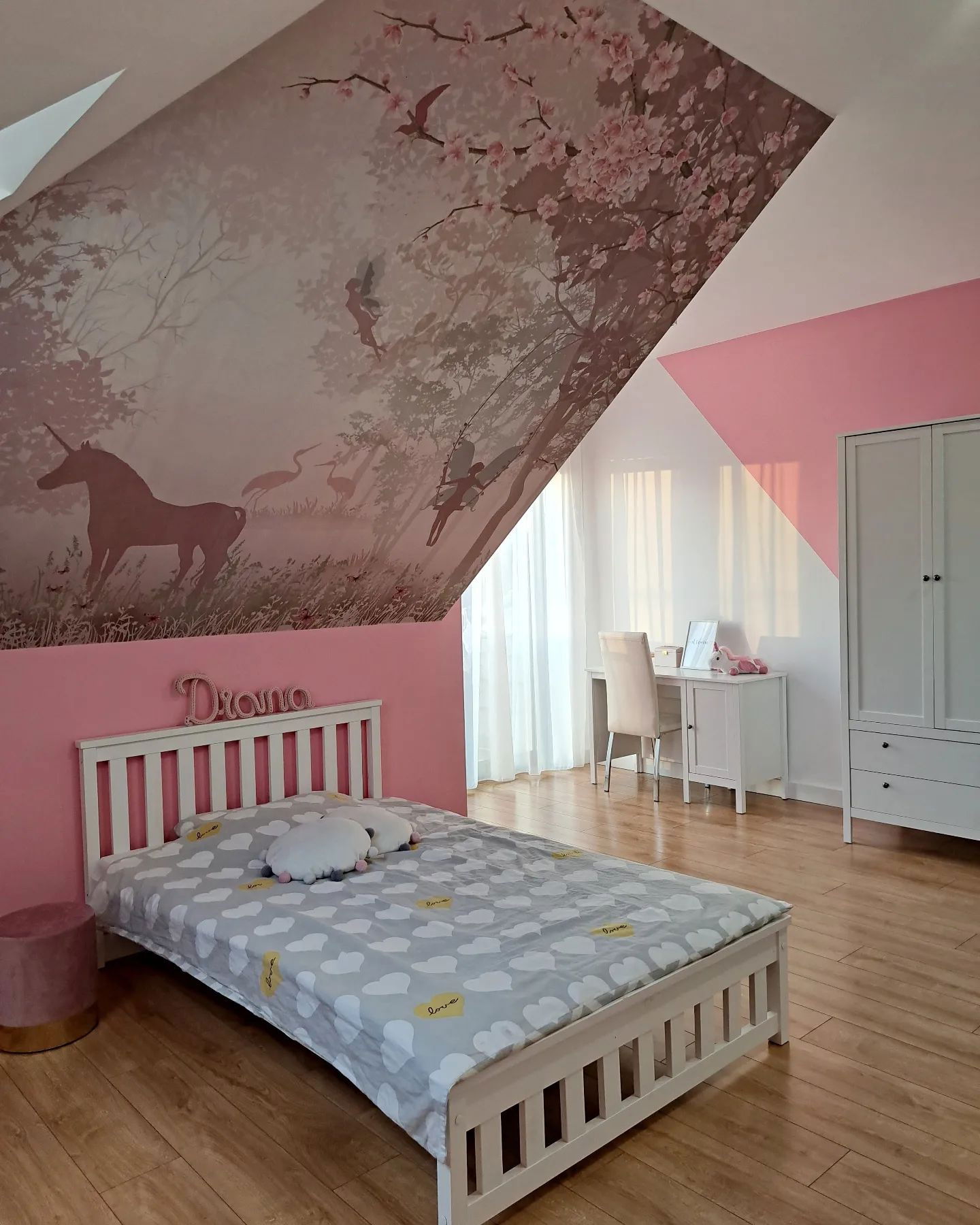 Child's bedroom with unicorn mural, white bed with cloud-patterned bedding, desk, and wardrobe.