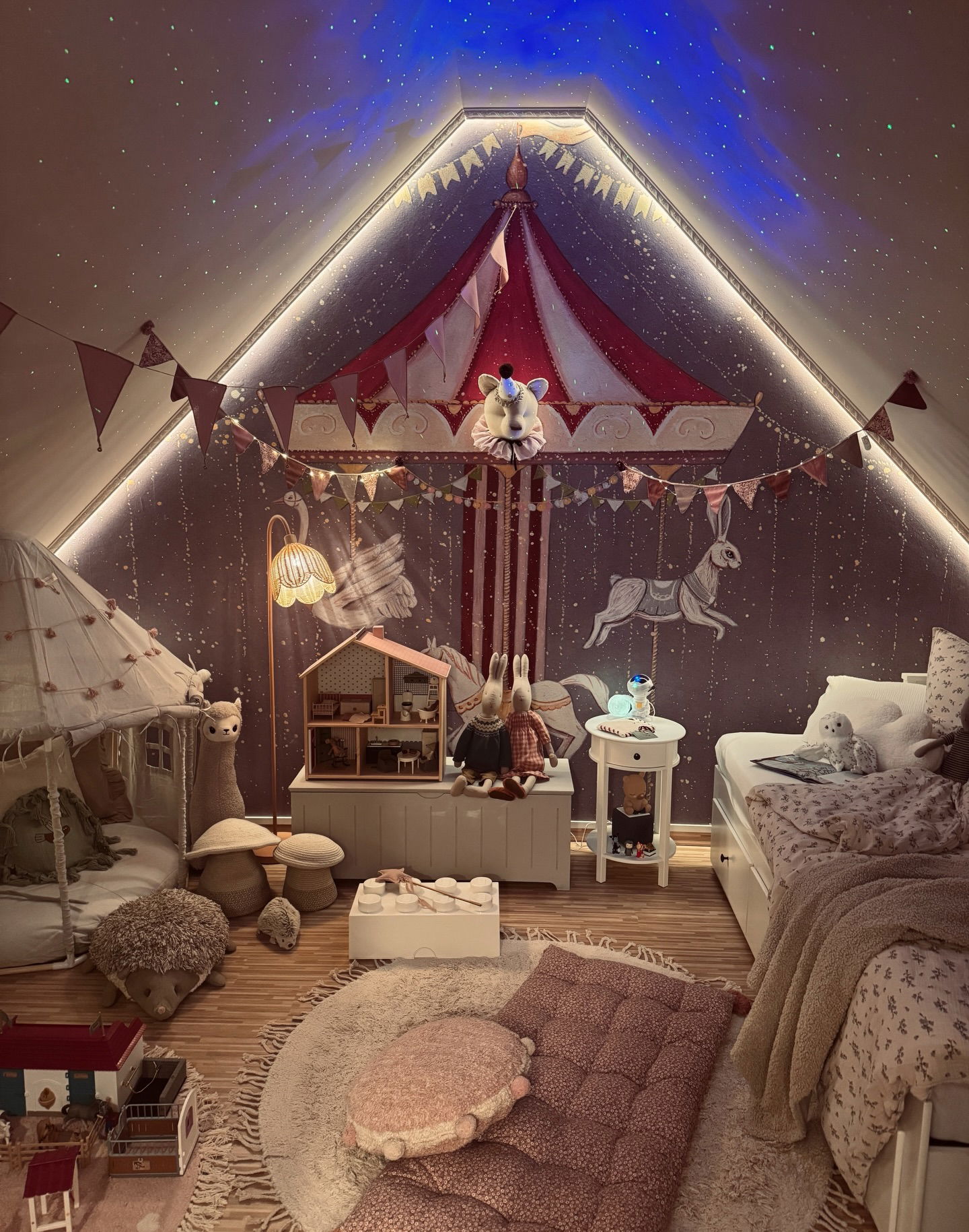 A child's whimsical room with a circus tent theme, featuring stuffed animals, a dollhouse, and a star-projected ceiling.